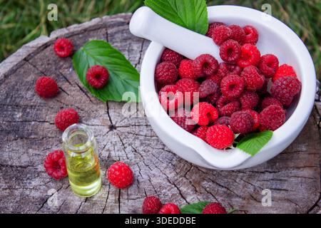 Olio essenziale di lampone in bottiglia con frutti di bosco freschi su un ceppo di legno Foto Stock