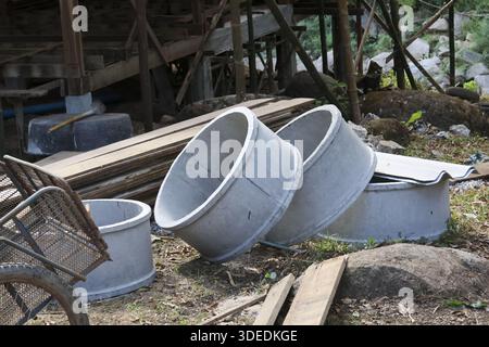 I tubi ad anello del pozzo di cemento e le tavole di legno sono abbandonati su terreni accidentati vicino al cantiere rurale, mostrando una scena tranquilla e deserta di W infinito Foto Stock