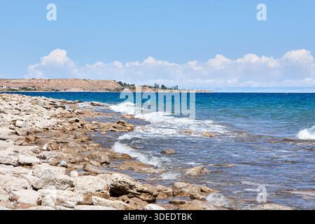 La costa rocciosa di un lago con onde che si infrangono dolcemente sulla spiaggia irregolare di pietra sotto un cielo azzurro e limpido, illustrando la bellezza naturale della costa. Foto Stock