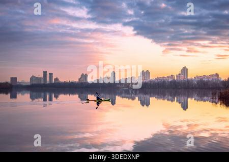 Tramonto sull'argine di Obolon a Kiev con moderno skyline residenziale che si riflette nelle calme acque del fiume, nelle spettacolari nuvole e nella luce calda Foto Stock