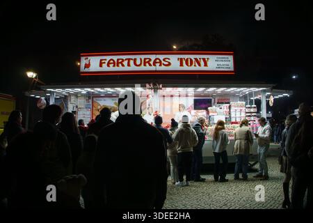La gente si riunì di notte di fronte a un chiosco di cibo luminoso chiamato Farturas Tony che vendeva dolci e spuntini a una fiera o a un festival Foto Stock
