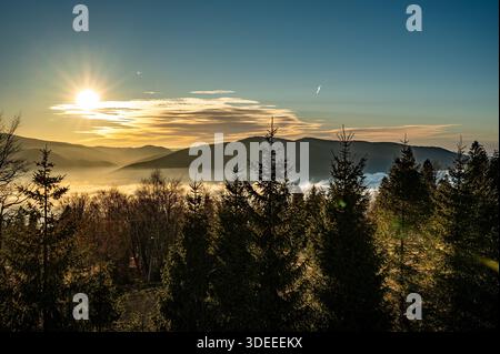 Sunset from Magurka Wilkowicka reveals a breathtaking panorama: the sun dips behind the silhouettes of Skrzyczne, Szyndzielnia, and Klimczok Foto Stock