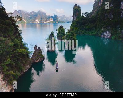 Annidato nel Parco Nazionale di Khao Sok, il Lago Cheow LAN offre splendide formazioni carsiche calcaree e acque cristalline. Una piccola barca scivola attraverso il tranquillo paesaggio, mostrando la natura incontaminata della bellezza. Foto Stock