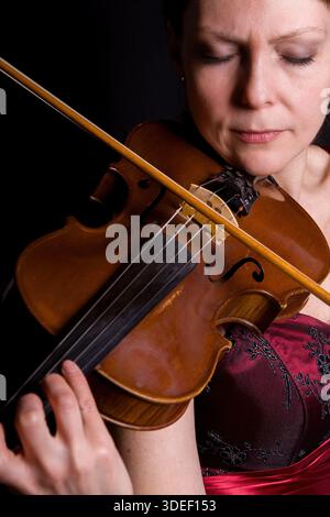 Una giovane donna suona la viola su sfondo nero Foto Stock