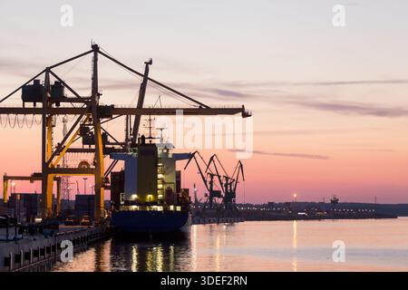 Sagoma di una nave portacontainer ormeggiata accanto alle gru portacontainer nel porto al tramonto, Klaipeda, Lituania Foto Stock