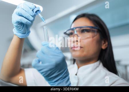 Una scienziata asiatica professionista lavora in un laboratorio moderno, conducendo test e analizzando campioni con precisione. Foto Stock
