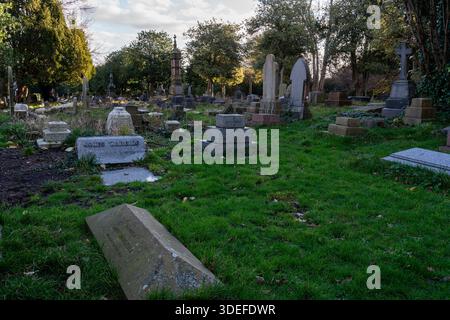 Lapidi e memoriali sparsi nel cimitero di Flaybrick con erba e alberi sotto la luce soffusa del giorno Foto Stock