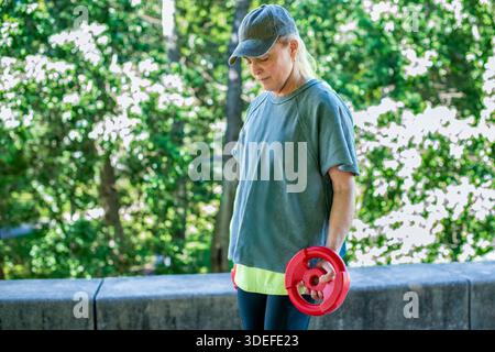 Donna di mezza età che si allena con pesi rossi in un parco all'aperto Foto Stock