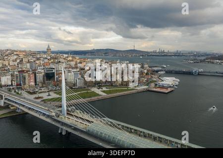 Vista aerea del ponte Halic Metro che si estende attraverso le tranquille acque del Corno d'Oro verso la storica Torre Galata sotto un cielo spiovente, i Foto Stock