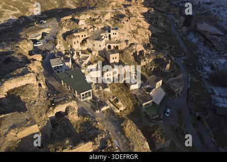Vista aerea di antiche abitazioni annidate nel paesaggio aspro e baciato dal sole, Cappadocia, Turkiye. Foto Stock