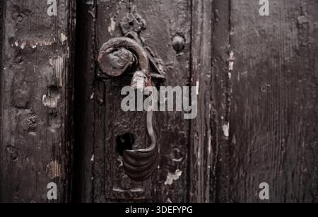 Primo piano di una vecchia maniglia in metallo rustico su una porta in legno resistente agli agenti atmosferici. Struttura vintage, architettura storica e concetto di superficie invecchiata. Foto Stock