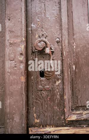 Primo piano di una vecchia maniglia in metallo rustico su una porta in legno resistente agli agenti atmosferici. Struttura vintage, architettura storica e concetto di superficie invecchiata. Foto Stock