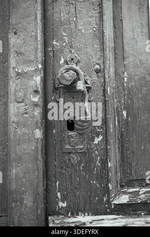 Primo piano di una vecchia maniglia in metallo rustico su una porta in legno resistente agli agenti atmosferici. Struttura vintage, architettura storica e concetto di superficie invecchiata. Foto Stock