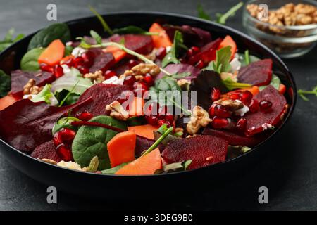 Deliziosa insalata con barbabietole, spinaci, rucola, formaggio, noci, semi di carota e melograno sulla tavola nera, primo piano Foto Stock
