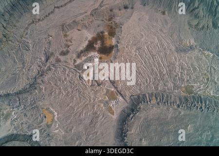 Vista aerea dall'alto verso il basso dei fanghi grigi essiccati con una rete di crepe e consistenze ruvide. Il desolato paesaggio industriale assomiglia a un letto di lago in pelo, cemento incrinato o una superficie lunare, che illustra la siccità e l'inquinamento. Foto Stock