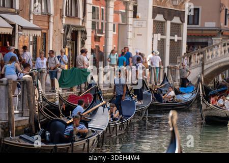 VENEZIA, ITALIA - 20 GIUGNO 2025: Vista ravvicinata di un vivace punto di imbarco della gondola. I gondolieri con le tradizionali uniformi a strisce sono visti gestire t Foto Stock