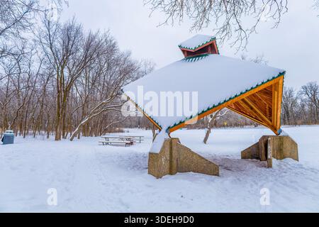 Riparo per picnic nel parco coperto di neve. Parco invernale con riparo per picnic in legno ricoperto di neve fresca. Area ricreativa all'aperto vuota con alberi e picnic Foto Stock