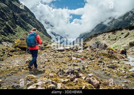 Donna con zaino e pali da trekking vestita di giacca softshell rossa durante il trekking nel Parco Nazionale di Makalu Barun in Nepal. Escursioni in montagna e persone attive Foto Stock