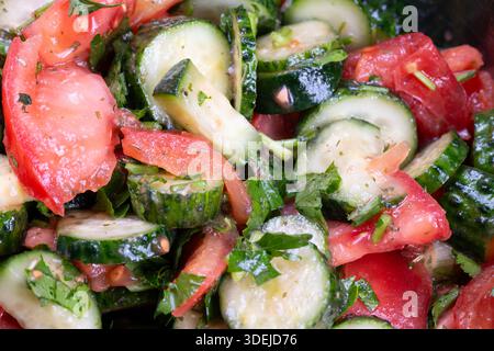 insalata di cetrioli di pomodoro fresco con erbe, olio di girasole luccicante, prezzemolo tritato e erba cipollina, primo piano della ciotola rustica, vivace contrasto rosso e verde, tex Foto Stock