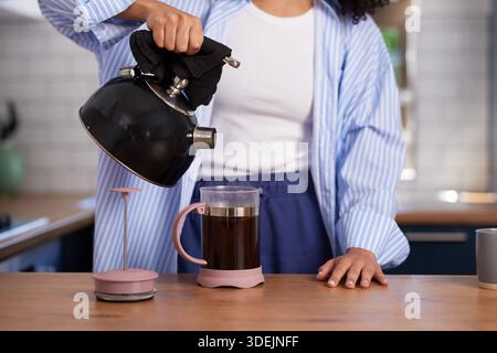 Persona che versa acqua calda dal bollitore alla macchina per il caffè Pink French Press nella cucina moderna Foto Stock