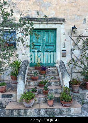 Porta di legno verde intemprata su scale di pietra decorate con vari vasi di fiori in ceramica a Matera. Foto Stock