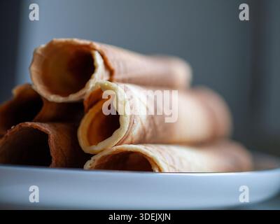 Coni laminati impilati su un piatto bianco con messa a fuoco morbida e sfondo blu tenue, natura morta degli alimenti minimalista. Foto Stock