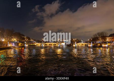 Parigi, Francia - 31 dicembre 2025: Vista notturna del Pont des Arts fotografata dalla Senna a bordo di una crociera turistica sul fiume, che mette in risalto l'ico Foto Stock