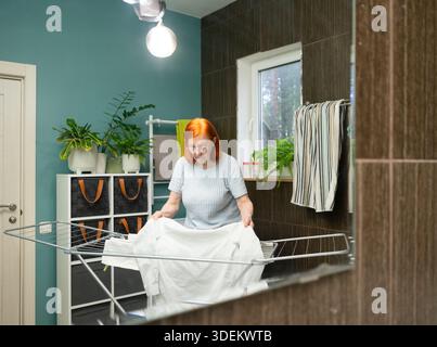 Una donna anziana raddrizza meticolosamente il tessuto dei suoi vestiti lavati su una griglia di asciugatura domestica per ottenere risultati di asciugatura senza pieghe. Foto Stock