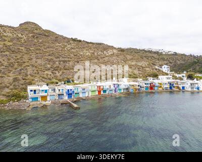 Vista aerea di un arcobaleno di barche annidato contro l'arida collina che incontra il mare turchese nel villaggio di pescatori di Klima, Milos, Grecia. Foto Stock