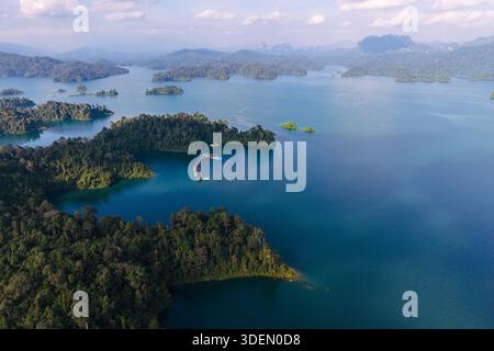 La splendida vista aerea del lago Cheow LAN rivela le sue acque color smeraldo circondate da vegetazione lussureggiante e scogliere calcaree. Esplora questo tranquillo paradiso perfetto per gli amanti della natura e dell'avventura. Foto Stock