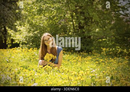 Bella ragazza seduta sul prato dei dandelions Foto Stock