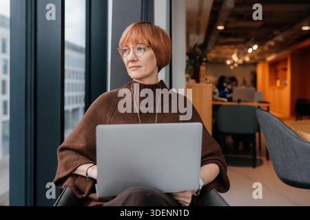 Imprenditrice donna che lavora in remoto su un notebook in un ufficio open space Foto Stock