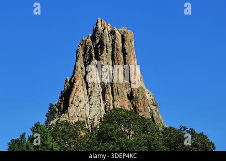La guglia rocciosa frastagliata si innalza ripidamente sulle cime verdi degli alberi al Garden of the Gods Park, Colorado Springs, Colorado, USA, isolata contro un cielo azzurro. Foto Stock