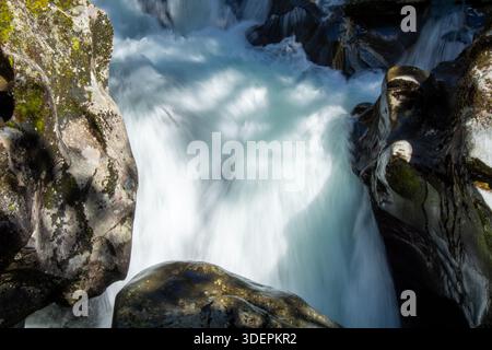 Una vista ravvicinata di una cascata che precipita su rocce lisce e scure. L'acqua appare bianca e schiumosa mentre scorre rapidamente, creando una a dinamica Foto Stock
