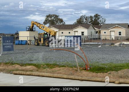 I lavoratori sono impegnati in un cantiere dove vengono costruite nuove case. I macchinari pesanti spostano i materiali mentre le recinzioni circondano l'area. Foto Stock