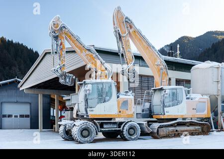 Vista panoramica escavatori idraulici congelati all'aperto condizioni invernali neve coperta ghiaccio industriale edificio alpino. Impatti a basse temperature Foto Stock