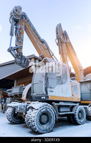 Vista panoramica escavatori idraulici congelati all'aperto condizioni invernali neve coperta ghiaccio industriale edificio alpino. Impatti a basse temperature Foto Stock