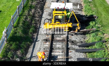 I lavoratori utilizzano una macchina specializzata per riparare i binari dei treni in condizioni di cielo limpido. Gli attrezzi e i nuovi materiali sono visibili in quanto garantiscono la sicurezza e il corretto funzionamento della ferrovia. Foto Stock