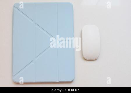 Vista dall'alto di un iPad azzurro su una scrivania bianca con un tablet e un mouse accanto, configurazione minima dello spazio di lavoro, tecnologia moderna e pulita. Foto Stock