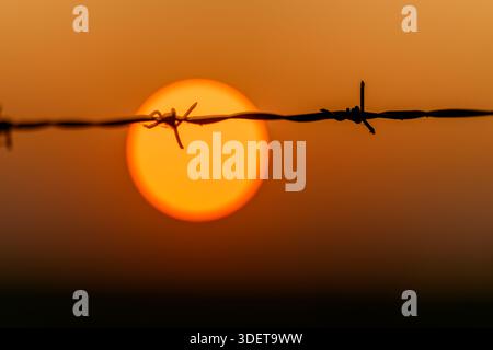 Uno splendido tramonto viene catturato attraverso il filo spinato, simboleggiando i confini e l'essenza della libertà Foto Stock