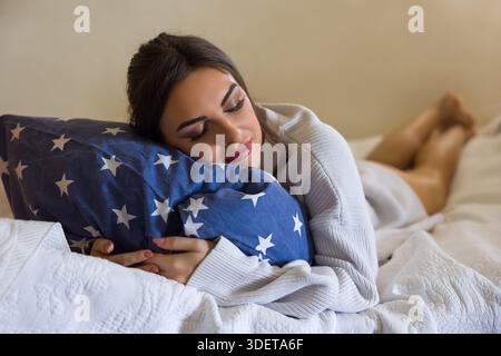 Bella giovane donna che indossa un maglione bianco chunky rilassante a letto Foto Stock