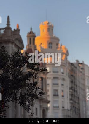 La luce dorata della sera illumina la parte superiore di una torre storica e di edifici residenziali ornamentali a Valencia, Spagna. Foto di alta qualità Foto Stock