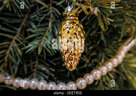 Ornamento a cono di pino dorato su un albero decorato di Natale e Capodanno con rami di abete verde e ghirlanda perla Foto Stock