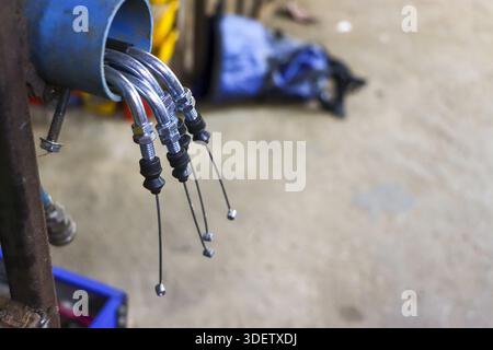 Espositore di pezzi di ricambio per motociclette appeso con filo del freno in acciaio e cavo della frizione che mostra i dettagli tecnici meccanici nell'officina di riparazione di officine automobilistiche con Foto Stock