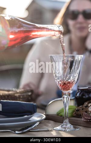 Versare vino rosato in un bicchiere di cristallo durante la cena all'aperto Foto Stock