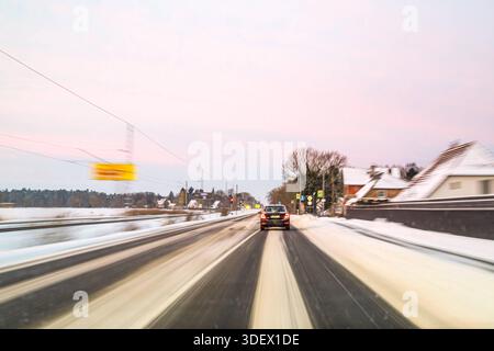 Rostock, Germania 09. Januar 2026: IM Bild: Ein Pkw fährt auf einer winterlichen Straße durch ein Ortsgebiet. Schnee und Matsch liegen auf der Fahrbahn, während durch eine lange Belichtungszeit Bewegungsunschärfen entstehen. DAS Bild verdeutlicht winterliche Verkehrsbedingungen, eingeschränkte Haftung und die Herausforderungen für Autofahrer bei Schnee und Glätte. Meclemburgo Vorpommern *** Rostock, Germania 09 gennaio 2026 nella foto Un'auto guida su una strada ventosa attraverso un'area locale neve e ghiaia giace sulla strada, mentre un lungo tempo di esposizione crea sfocature in movimento l'immagine illustra W Foto Stock