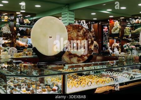 Grandi dischi bi-disc in giada e pietra lucidati dominano l'esposizione in una gioielleria luminosa. I banchi in vetro presentano ornamenti intagliati e bano circolare Foto Stock