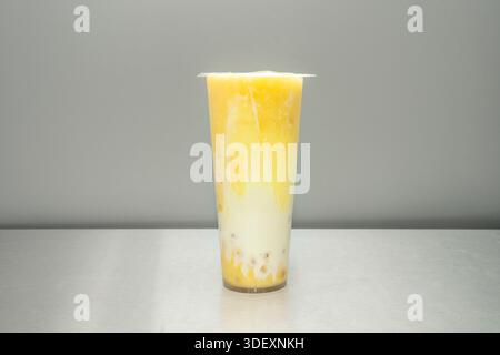 Una bevanda a base di tè al mango con veri pezzi di frutta sul fondo e una consistenza semi-solida, dove le perle di tapioca si fondono con la polpa di arancia brillante Foto Stock