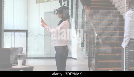 Donna che interagisce indossando il visore VR in un abbigliamento formale, gesti con le mani in ufficio, tazza di carta Foto Stock