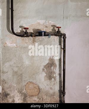Vecchi tubi idraulici contro una parete intemprata con vernice staccabile. Foto Stock